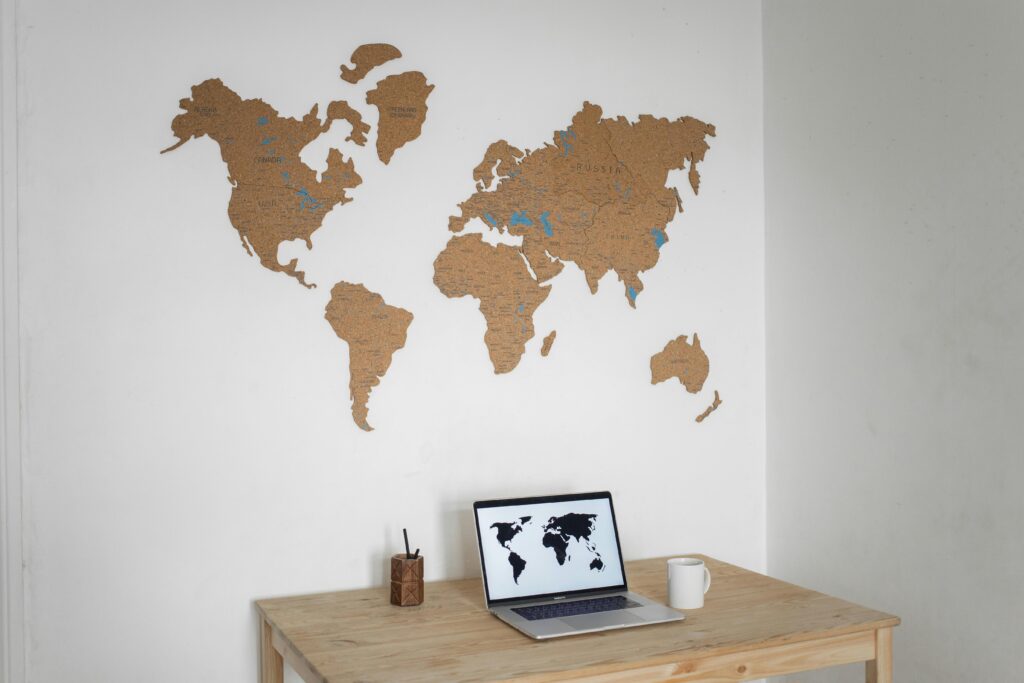 A minimalist workspace with a laptop and cork world map wall art.
